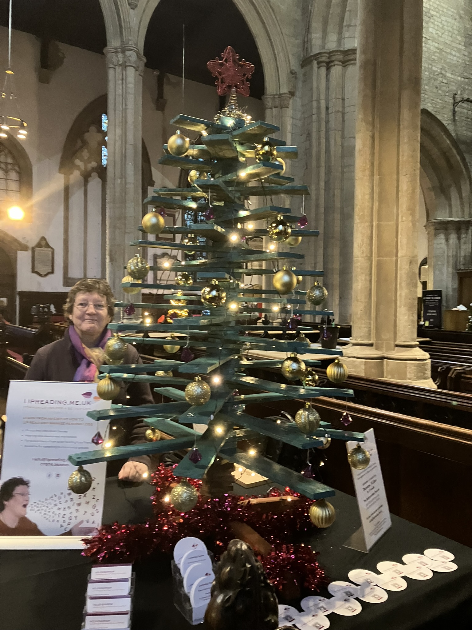 Picture of Helen with a wooden Christmas Tree and Lipreading.me.uk information about lipreading classes